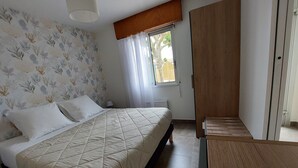 A bedroom with a bed, a wooden wardrobe, a window with curtains, and a wall with a leaf pattern.