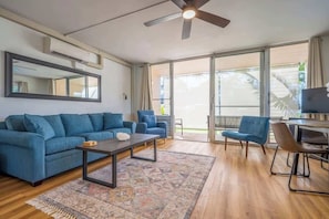 Un salon moderne comprenant un canapé, une table basse et des fauteuils, un ventilateur de plafond et une grande porte-fenêtre coulissante donnant sur un balcon.