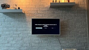 Una sala moderna con un televisor de pantalla plana montado en una pared de ladrillo, dos lámparas colgantes y una repisa con objetos decorativos.