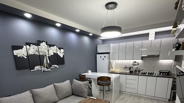 Una cocina moderna con armarios blancos, un comedor con mesa de madera y un sofá gris.