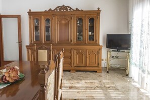 A dining area with a wooden dining table, chairs, a cabinet with glass doors, and a television on a stand. - S283 - Sirolo, large panoramic four-room apartment (Sirolo)