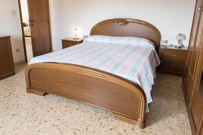 Ein Schlafzimmer mit einem hölzernen Bett, einem Nachttisch mit Lampe, einer Kommode und einer Tür.
