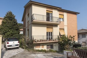 Ein zweistöckiges Gebäude mit Balkon, einem geparkten Auto und einer Bank.