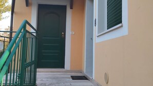 Un edificio con puerta verde, una escalera con barandilla verde y un ventanal con contraventanas verdes.