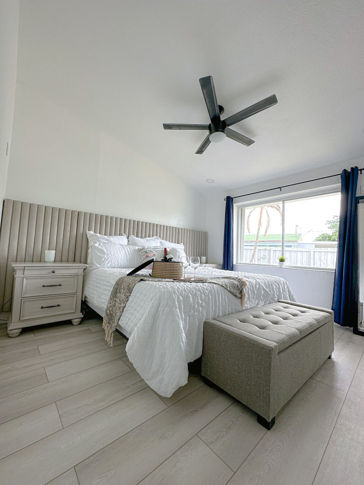 A bedroom with a bed, bedside table, nightstand, and a ceiling fan.