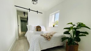 A bedroom with a bed, a window, a plant, and a door leading to another room. - Dream Vacation House 4B/2B Miami, FL (Hialeah)