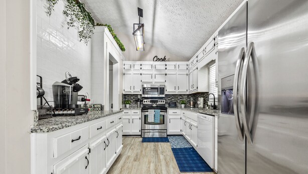 A modern kitchen with white cabinetry, stainless steel appliances, and a blue rug. - The Happy Place: 3BR in Quiet Neighborhood (Douglasville)