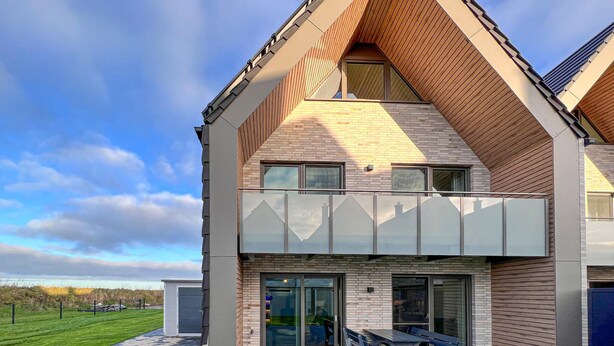A modern two-story house with a sloped roof, large windows, and a balcony. - Stunning home in Büsum with sauna (Büsum)