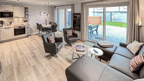 A modern living room with a sofa, chairs, a coffee table, and a dining area with a kitchen in the background. - Stunning home in Büsum with sauna (Büsum)