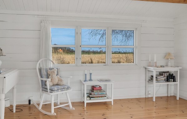 A room with a rocking chair, a small table with books and candles, and a window with a view of a field. - Nice home in Rødby with WiFi (Rødby)