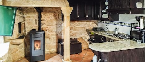 Una cocina rústica con pared de piedra, estufa de leña, armarios de madera oscura y salpicadero de azulejos.