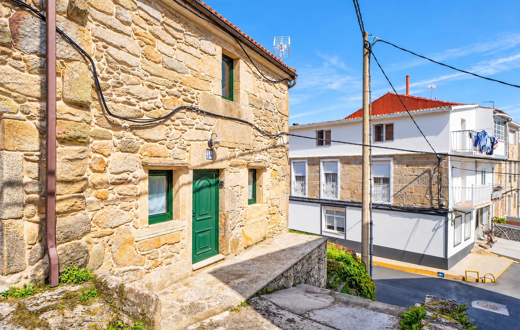 A stone building with a green door and a white building with balconies in the background.