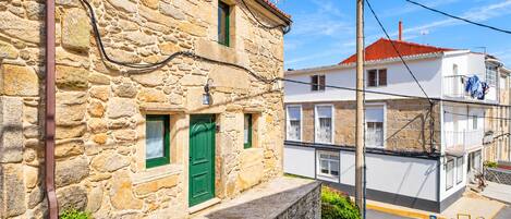 A stone building with a green door and a white building with balconies in the background.