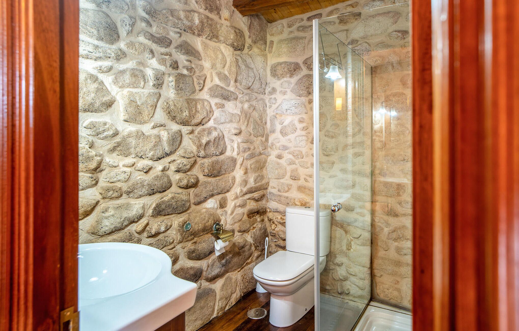 A bathroom with a stone wall, a white sink, and a glass shower enclosure.
