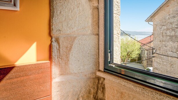 A stone wall adjacent to a window with a view of a building and a tree. - Lovely home in Muros with WiFi (Muros)