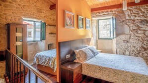 A bedroom with a stone wall, wooden ceiling beams, a bed with a floral bedspread, a nightstand, and a wooden wardrobe. - Lovely home in Muros with WiFi (Muros)