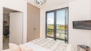 Ein Schlafzimmer mit Bett, Kleiderschrank, Fernseher und einem Balkon mit Blick ins Grüne.