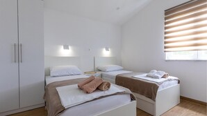 A modern bedroom with two beds, a wardrobe, and a window with blinds. - Stunning apartment in Komarna with WiFi (Komarna)