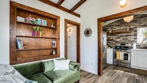 A living room with a green sofa, wooden shelves, and a kitchen visible through an open doorway. - J.T. Cottage (Yucca Valley)