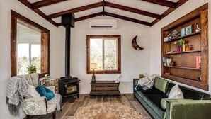 A cozy living room with a fireplace, a green sofa, a patterned armchair, and a wooden bookshelf. - J.T. Cottage (Yucca Valley)