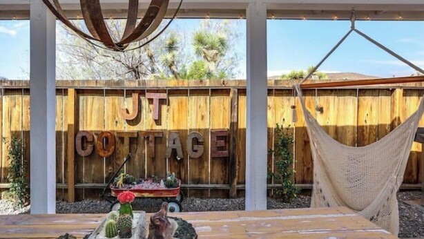 A wooden fence with "JT COTTAGE" written on it, a hammock, and a table with decorative items. - J.T. Cottage (Yucca Valley)