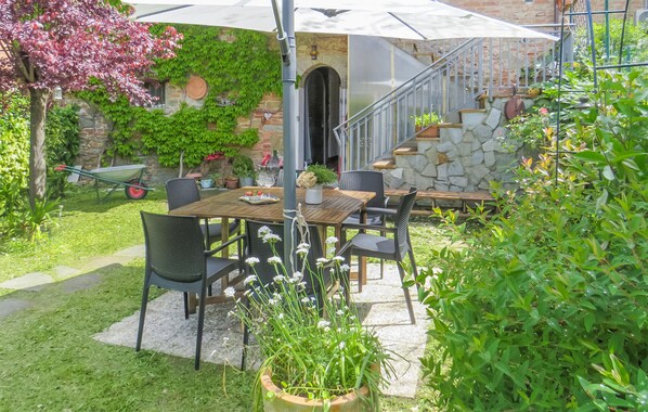 Une terrasse extérieure avec une table et des chaises en bois, entourée de plantes en pot et d’un mur de pierre.