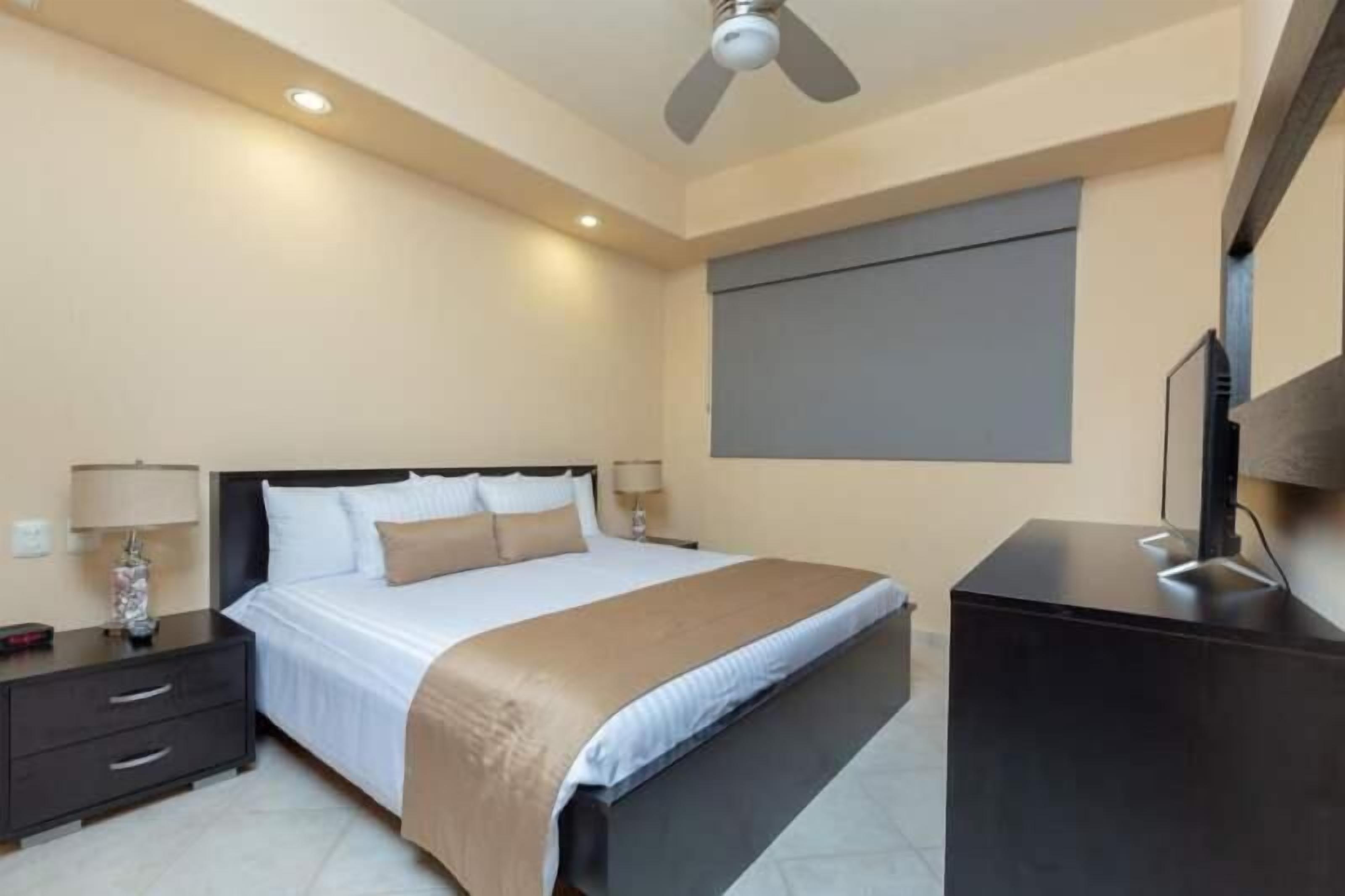 Une chambre d’hôtel équipée d’un lit, de tables de chevet, d’un bureau, d’un ventilateur de plafond et d’une télévision.