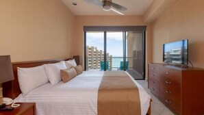 Habitación de hotel con cama, televisor, cómoda y balcón con vistas.