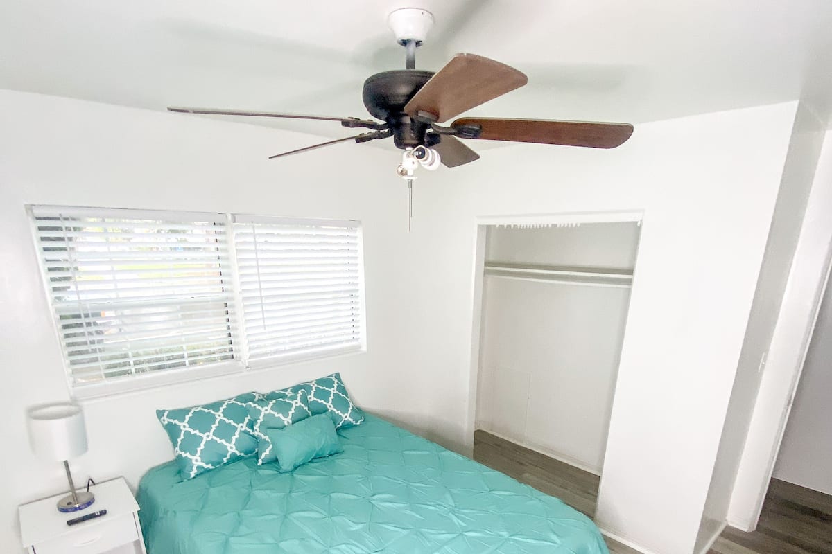 A bedroom with a bed, a nightstand, a ceiling fan, a window with blinds, and a wardrobe.