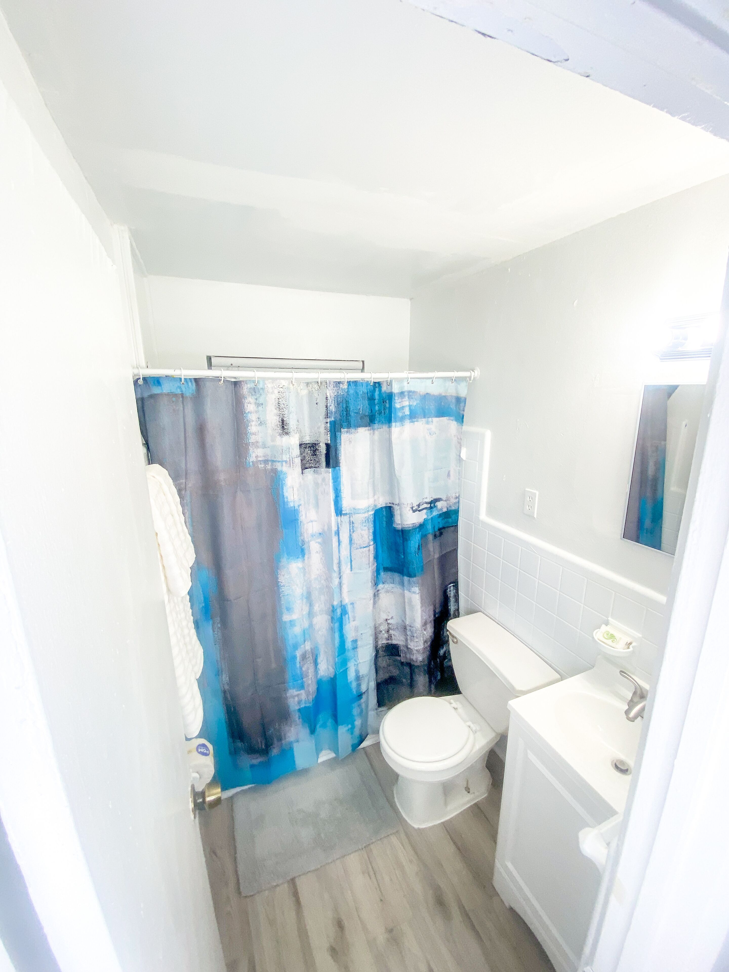 A bathroom with a shower curtain, toilet, sink, and mirror.