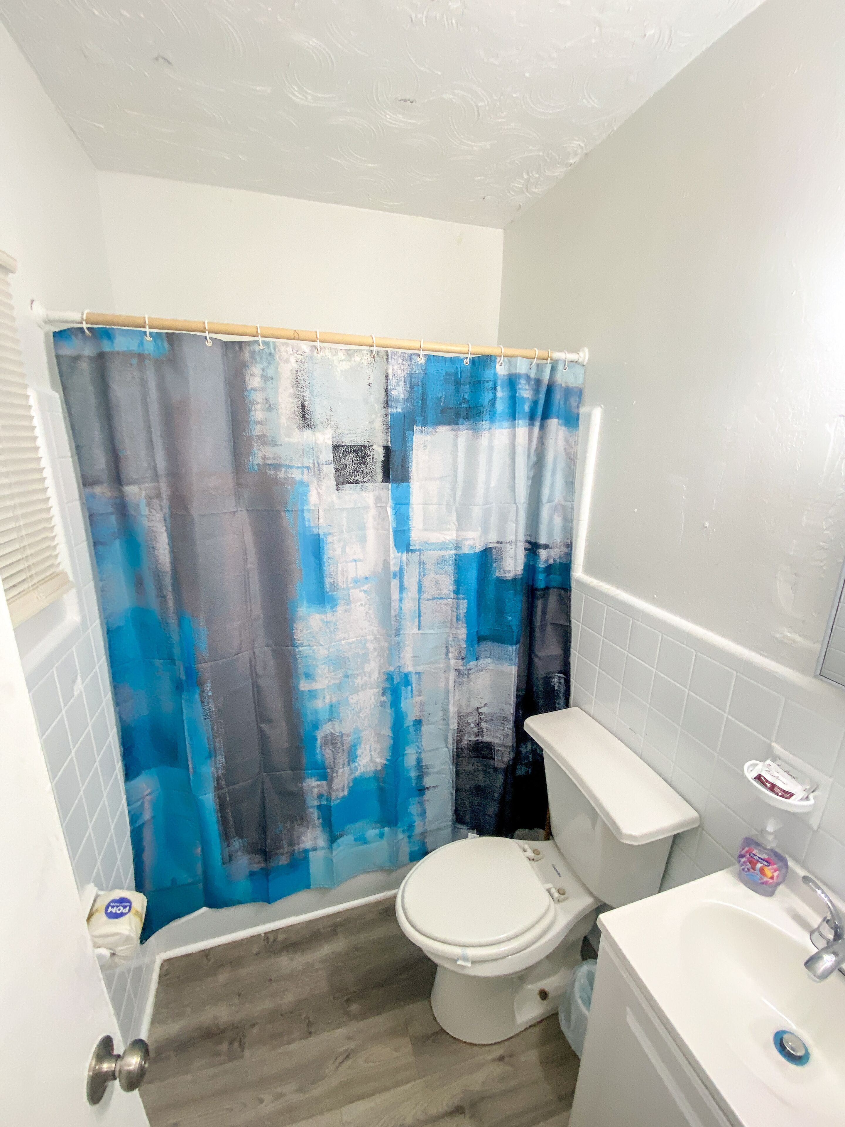 A bathroom with a shower curtain, toilet, sink, and a small shelf with toiletries.