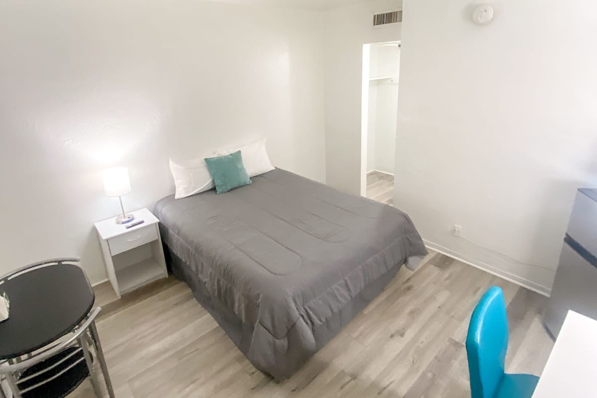 A small, neatly arranged bedroom with a bed, bedside table, chair, and a desk.