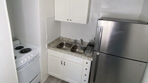 A compact kitchen with white cabinets, a stainless steel refrigerator, a double sink, and a stove. - Uptown Suites (St. Petersburg)