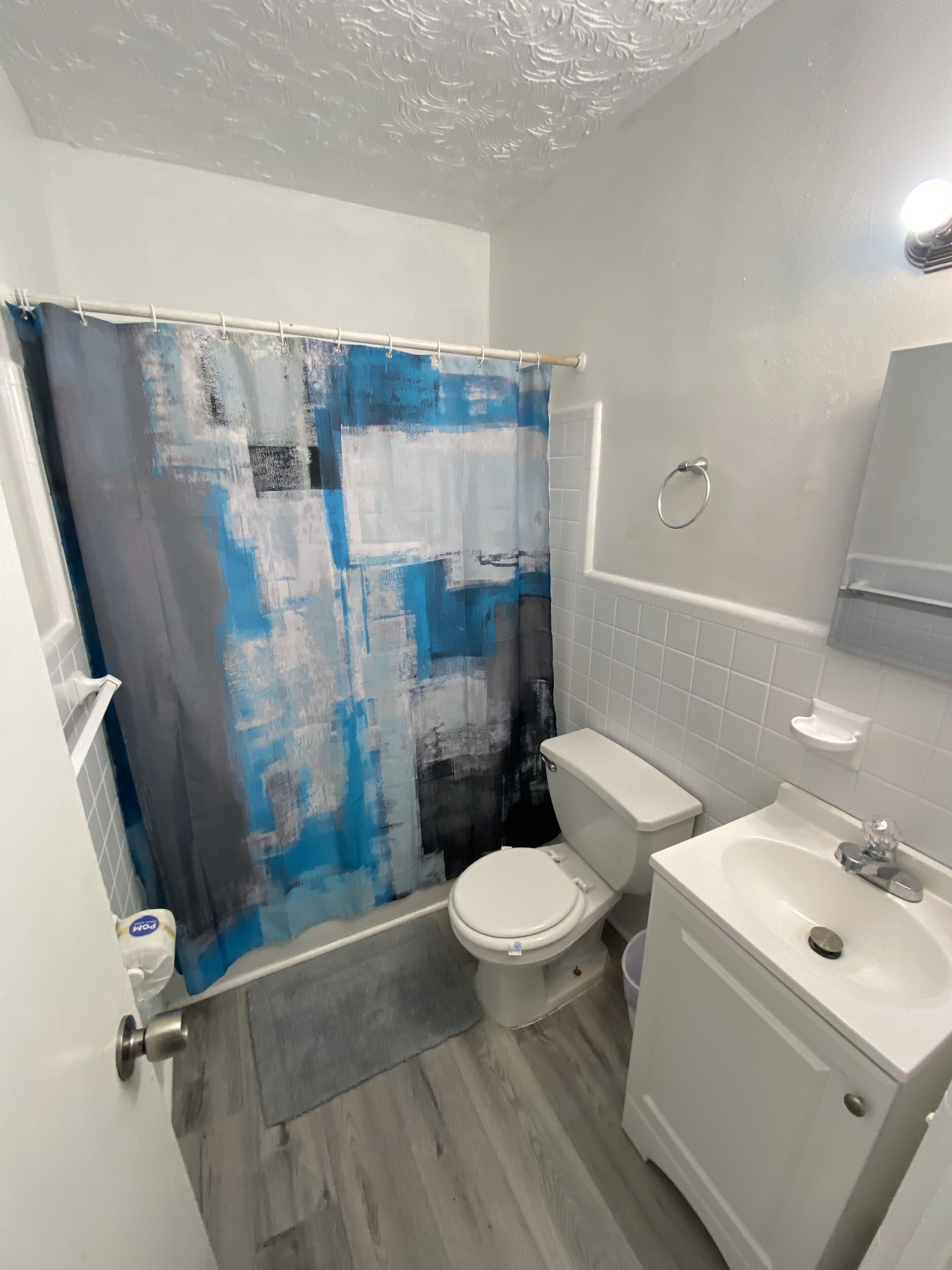 A bathroom with a shower curtain, toilet, sink, and a towel rack.