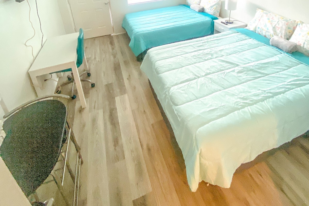 A room with two beds, a desk, a chair, and a TV.