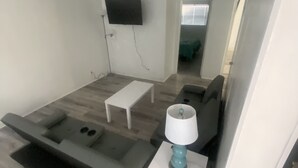 A modern living room with a sofa, a coffee table, a TV mounted on the wall, and a small side table with a lamp. - Uptown Suites (St. Petersburg)