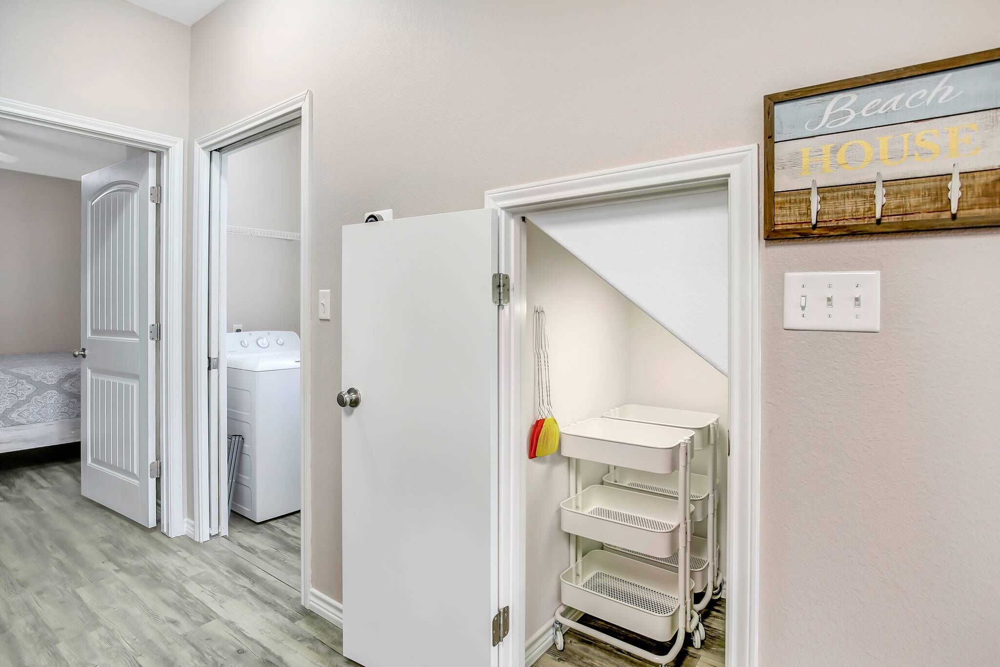 A laundry room with a washing machine and dryer, a utility closet with shelves, and a sign that reads 'Beach House'.