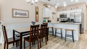 A kitchen with white cabinets, a large island, and a dining area with wooden chairs.
