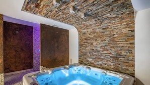 Une salle de spa moderne avec un mur en pierre, un jacuzzi et un mur éclairé de lumière violette.