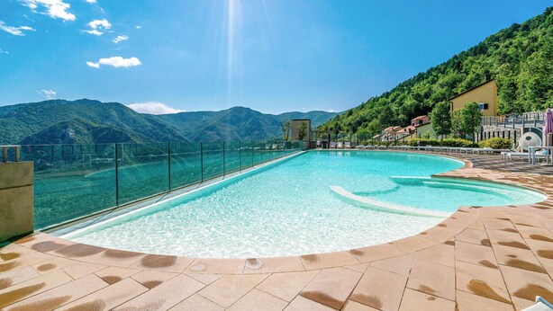 Une piscine à l’eau claire, entourée d’une terrasse carrelée, et offrant une vue sur un paysage montagneux.