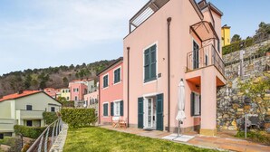 Une villa rose dotée d’un balcon, d’un mur en pierre et d’une pelouse verdoyante.