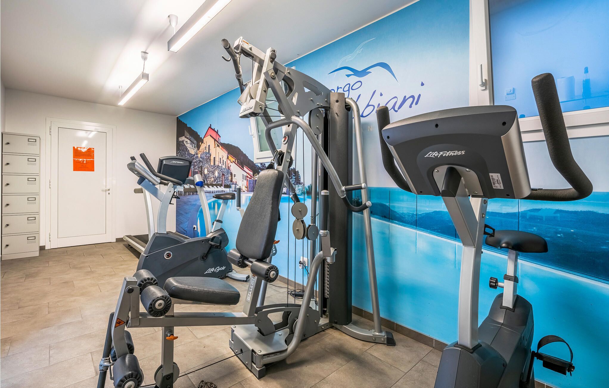 A gym with cardio machines, weight equipment, and a mural on the wall.