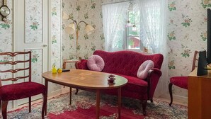 A room with floral wallpaper, a red velvet sofa, a wooden table, and a vintage clock. - Stunning home in Eringsboda with sauna (Eringsboda)