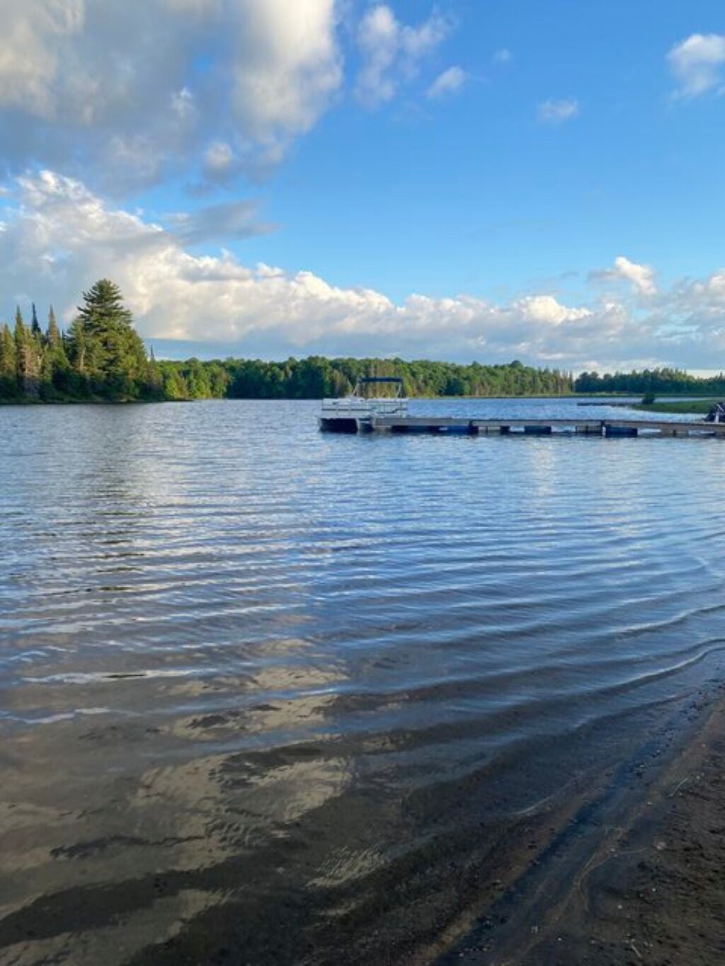 A calm lake with a dock extending into the water, surrounded by dense forest.