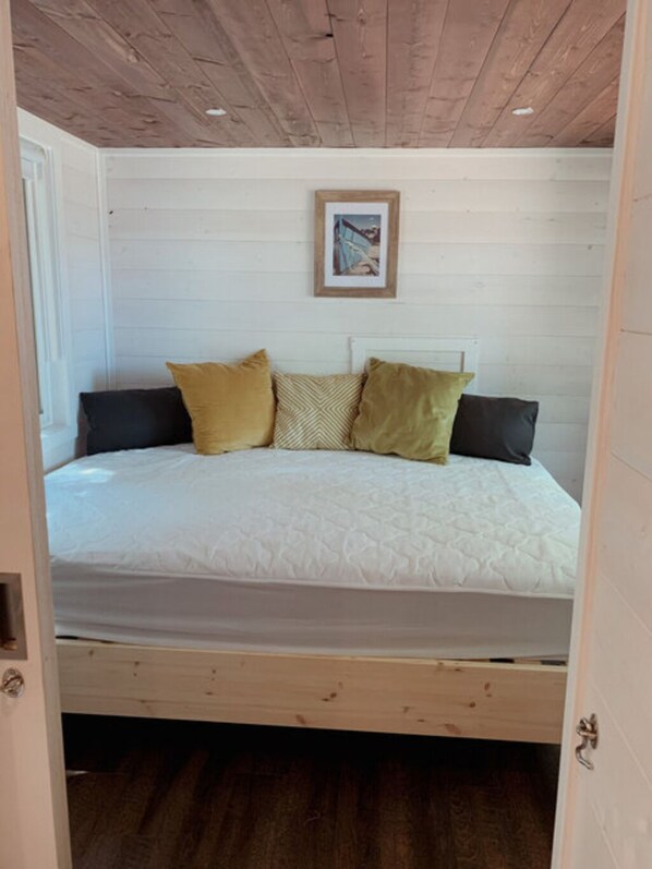Een bed met witte beddengoed, meerdere kussens en een ingelijste foto aan de muur erboven.