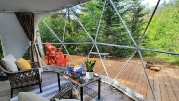 A cozy interior with a large window, wicker furniture, and a small table with decorative items. - Site #8 | Terra Dome (Whitestone)