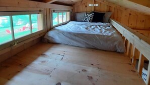 Un dormitorio acogedor en el ático con techo inclinado de madera, una cama individual con almohadas y un gran ventanal con vistas al exterior.
