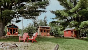 Un alojamiento de estilo rústico tipo cabaña con dos cabañas y un edificio central, rodeado de árboles y un patio cubierto de césped.