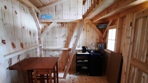 Interior de una cabaña de madera con una mesa de comedor, sillas, una cocina y una escalera.