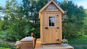 Una cabaña de madera con un letrero que dice "The Woodes Thoreau". Tiene una puerta principal, una ventana pequeña y un juego de escalones de madera que conducen a ella.